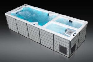 Large rectangular hot tub with multiple seating sections and blue water, surrounded by gray paneling.