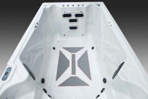 Empty white hot tub interior with multiple jet outlets at the far end and a geometric gray logo on the floor.