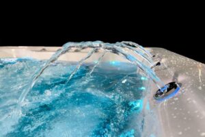 Hot tub with blue illuminated water jets arching over turquoise water in a bubbly spa setting.