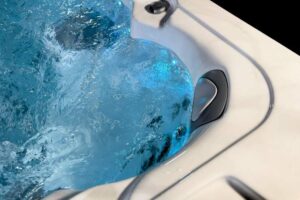 Close-up of a bubbling blue hot tub with a white acrylic edge and a built-in jet control panel nearby.
