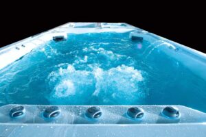 White hot tub filled with blue bubbling water, viewed from the near rim showing control knobs along the edge.