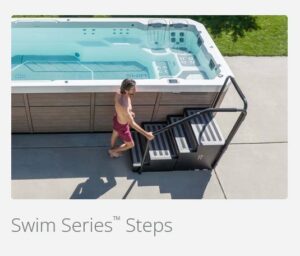 Person in a red swimsuit uses metal pool steps beside a rectangular blue pool, viewed from above.