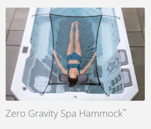 Child in a blue swimsuit floating in a zero-gravity spa hammock inside a hot tub.