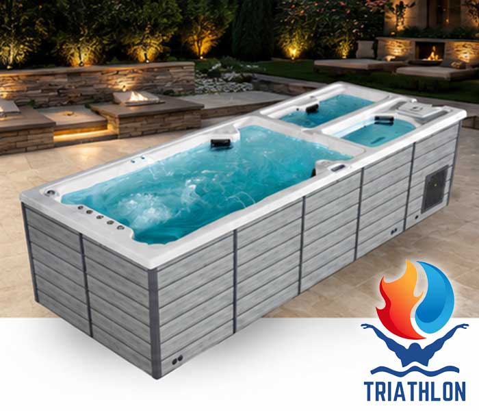 Outdoor rectangular hot tub with two connected sections and bubbling blue water on a stone patio, Triathlon logo in the bottom-right corner.