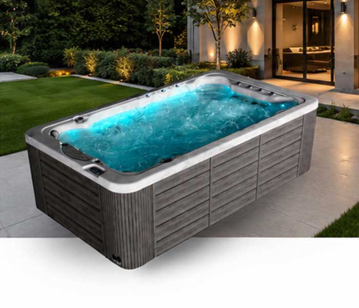 Outdoor rectangular hot tub with blue-lit water, surrounded by dark wooden panels in a modern backyard. Written lighting suggests evening time.