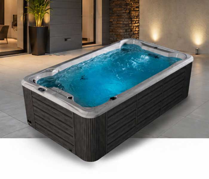 Rectangular outdoor hot tub filled with blue water on a tiled patio beside a modern house exterior.