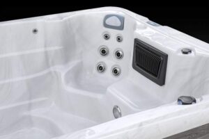 White fiberglass hot tub interior with multiple jet nozzles and built-in rectangular vent panel on the side edges, showing seating and controls nearby.