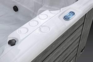 White hot tub edge with a built-in digital control panel and visible jet buttons on a wooden deck exterior