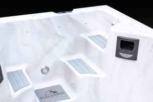 White hot tub interior with blue-striped non-slip steps and built-in seating, a drain, and an Icelandic Swim panel on the deck.