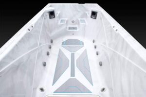 White boat deck interior seen from the bow, featuring blue-gray geometric non-slip pads and fixtures along the sides against a dark background.