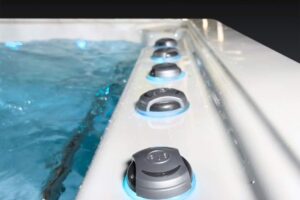 Close-up of black and blue control knobs along a hot tub edge, water visible on left side.