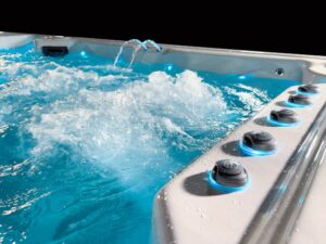 Hot tub with blue water and multiple black jet dials along the edge, creating splashes and bubbles in motion.