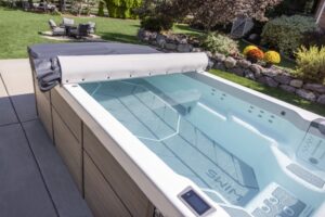 Outdoor hot tub with a gray rolled-back cover on a wooden deck in a sunny backyard garden.