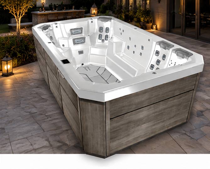 White outdoor hot tub with multiple built-in jets and seating for several people, set on a stone patio with warm lantern lighting and a wooden exterior paneling.