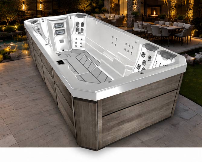 Outdoor rectangular hot tub with white interior and wood-gray exterior on a tiled patio at dusk/night nearby lounge area.